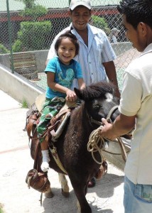 A child rides on a pony smiling with assistant.